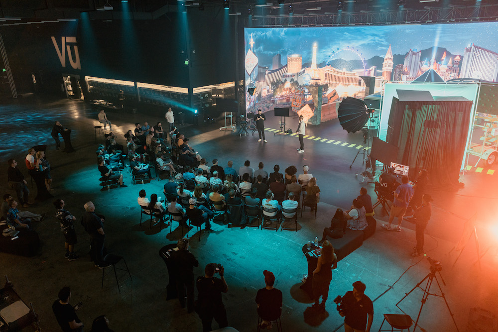 An AI-assisted post-production studio featuring the application of adaptive visual effects and voice cloning. The image shows a post-production specialist working on a high-resolution monitor, using AI tools like Gen-1 by Runway and Respeecher to enhance video consistency and create realistic voiceovers for a virtual character. The screen displays a split image showing the original footage and the AI-enhanced version, highlighting the improvements in visual effects and the consistency achieved through AI. The background features a voice-over booth where audio engineers fine-tune the synthesised voice to match the emotional tone of the character. This visual captures the role of AI in adding creative depth and efficiency to post-production, ultimately elevating the storytelling quality